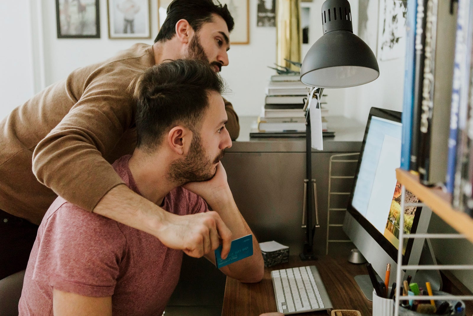 Gay couple shopping online through credit card on computer at home