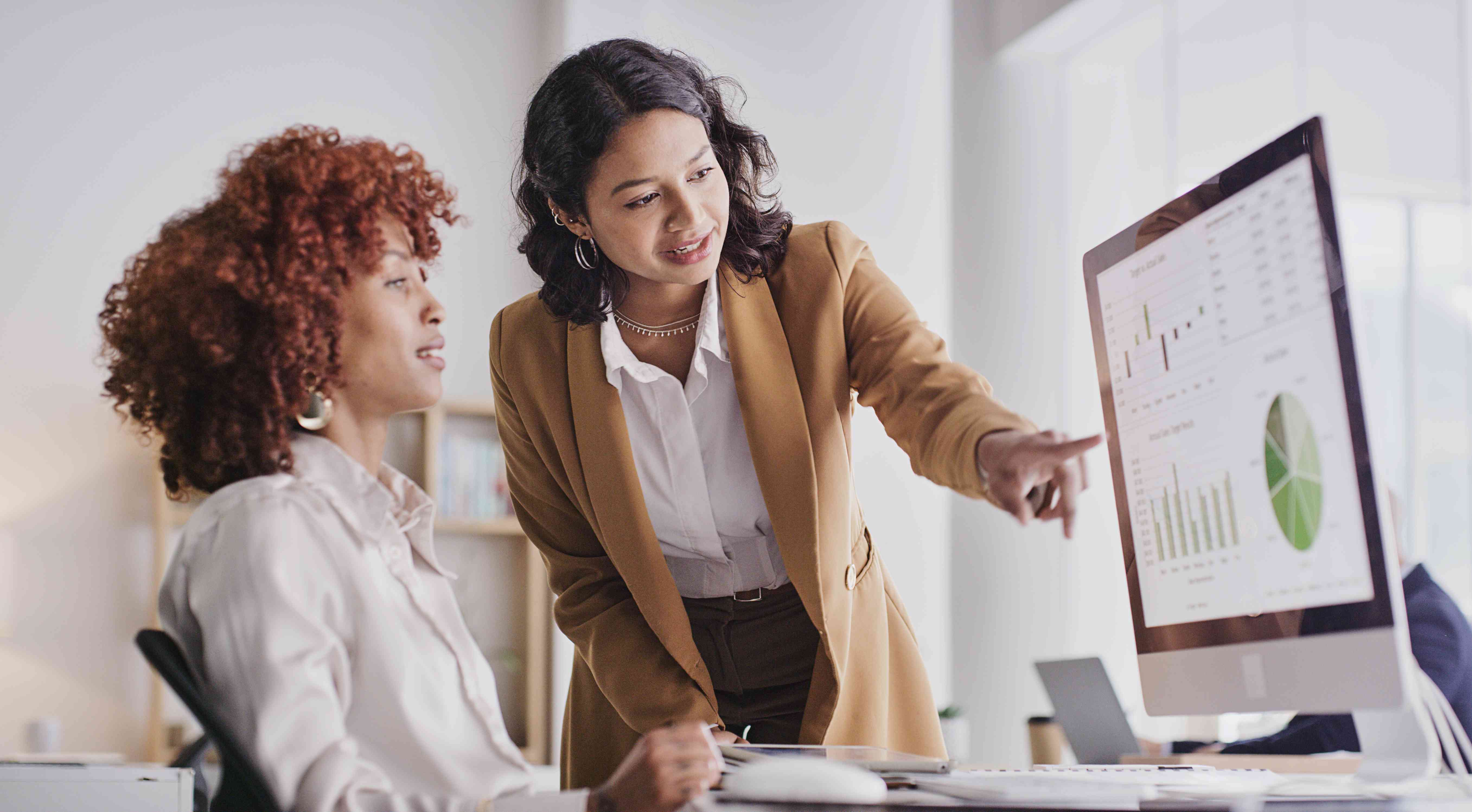 Two woman looking at graphs and other data on a computer